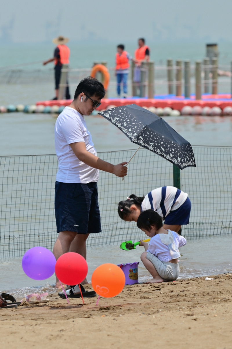 《烈日下》2021年5月1日，广州南沙区天后宫沙滩，烈日下一位爸爸为女儿打伞遮阳。苏裔燕摄.JPG